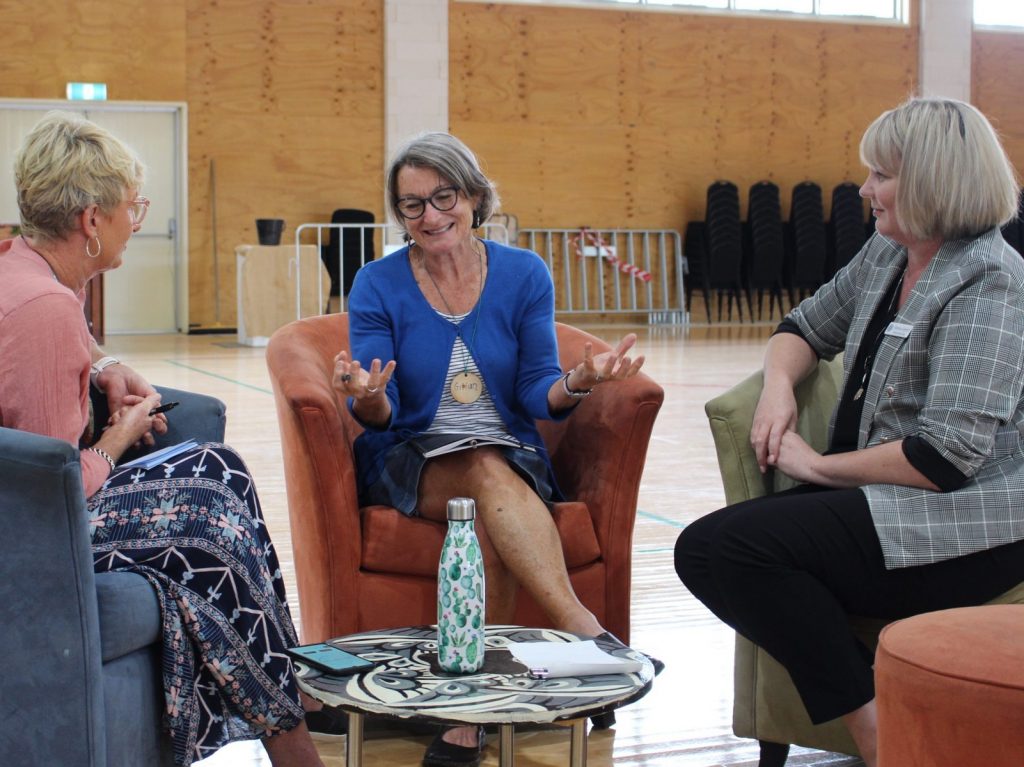 three women sitting in chairs in a circle speaking together