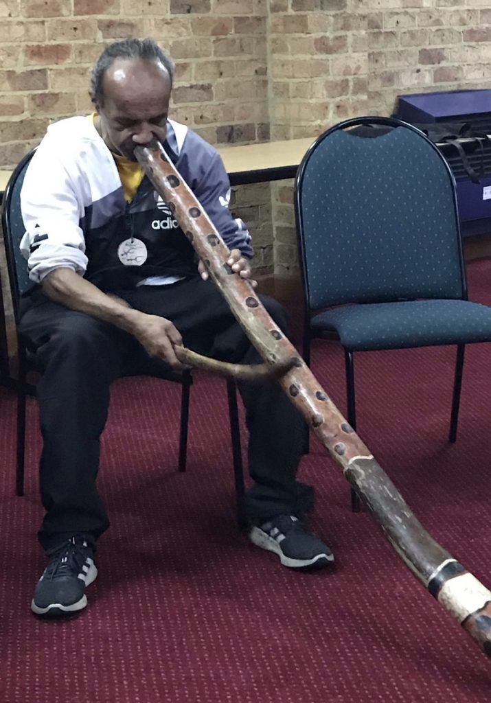A first nations community member playing the Digeridoo
