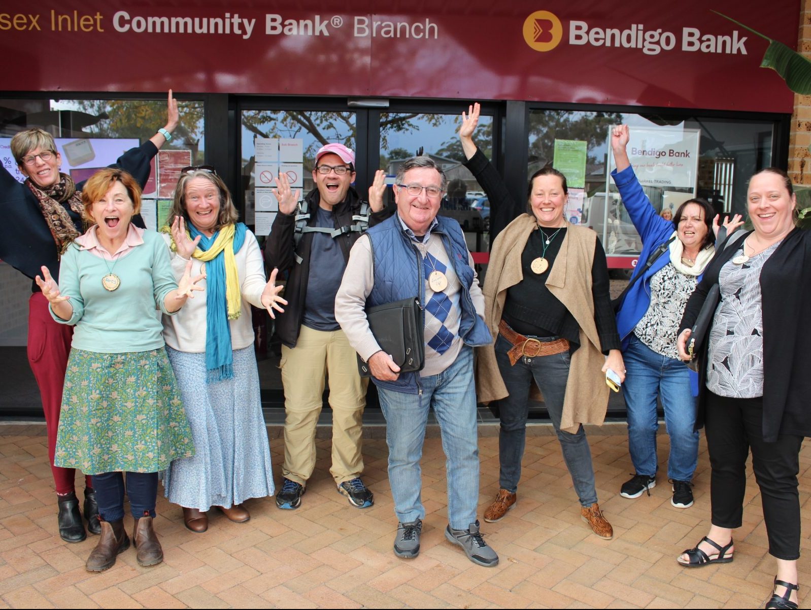 Group shot of 8 people cheering in front of Bendigo Bank